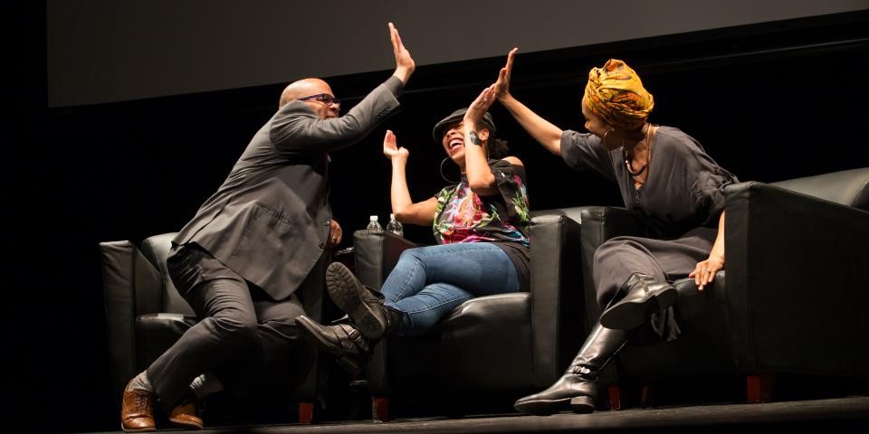 Three people onstage at the Schomburg Center laugh and give each other high-fives.