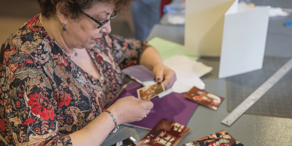 A woman looks at a photograph while in the midst of creating a scrapbook. 